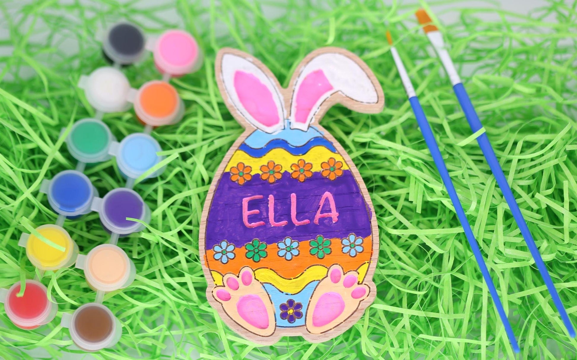 Easter egg paint craft kit with paint pots, paintbrushes and personalized Easter egg painted with bunny ears and bunny feet.
